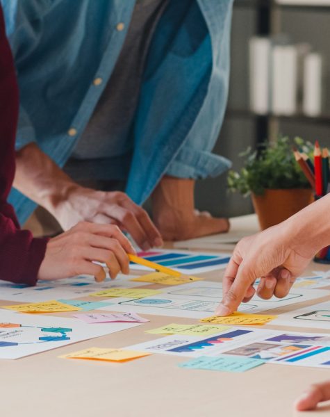 Asian businessmen and businesswomen meeting brainstorming ideas about creative web design planning application and developing template layout for mobile phone project working together in small office.